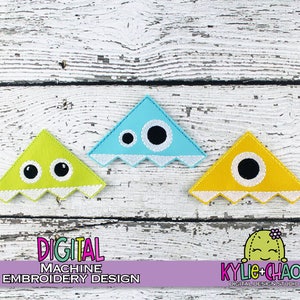 May include: Three colorful, triangular digital machine embroidery designs. The designs feature cartoon monster faces in yellow, light blue, and green, with black eyes and white jagged edges. The text "DIGITAL MACHINE EMBROIDERY DESIGN" is visible.