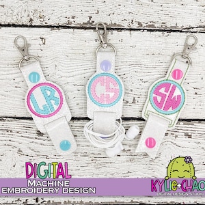 May include: White earbud holders with a silver clasp and a button closure. Each holder features a monogram in a circle, with the initials "LR", "GS", and "SW" embroidered in pink and blue. The text "DIGITAL MACHINE EMBROIDERY DESIGN" is at the bottom.