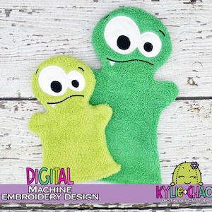 Puede incluir: Dos marionetas de mano de monstruos verdes. Las marionetas tienen ojos blancos grandes con pupilas negras, una boca cosida y brazos pequeños. El texto "DIGITAL MACHINE EMBROIDERY DESIGN" es visible en la imagen. Están hechas de un material suave y afelpado.