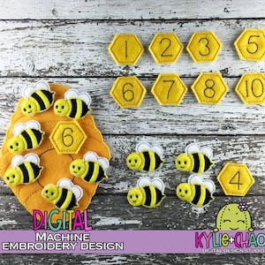 May include: A felt educational toy set featuring a beehive, bees, and numbered honeycomb shapes. The bees are yellow and black with white wings. The honeycomb shapes are yellow with black numbers 1-10. The text "DIGITAL MACHINE EMBROIDERY DESIGN" is visible.