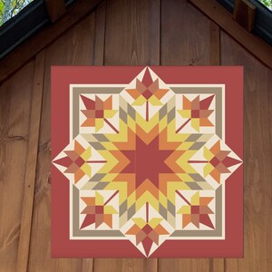 May include: A geometric quilt design featuring a central eight-pointed star in shades of yellow, orange, and red, surrounded by stylized leaf shapes. The quilt is framed by a red border and set against a wooden background.