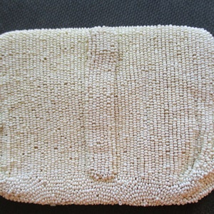 May include: A white beaded clutch bag. The bag is made of small, round beads that are sewn together to create a smooth, textured surface.