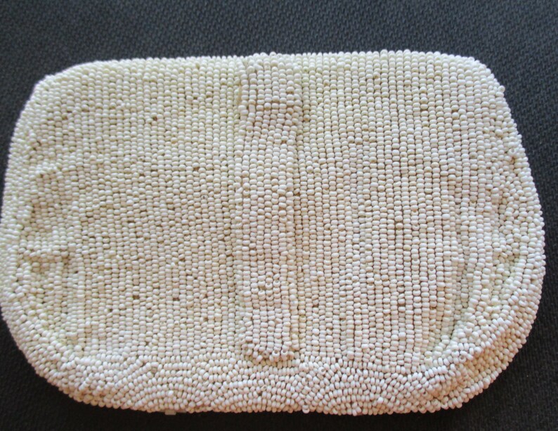 May include: A white beaded clutch bag. The bag is made of small, round beads that are sewn together to create a smooth, textured surface.