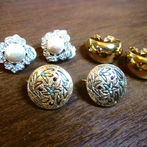 May include: A set of four gold-tone earrings. Two earrings feature a floral design with red and turquoise accents. The other two earrings are simple hoops.