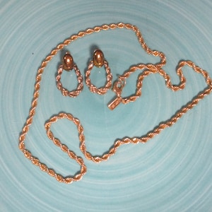 May include: A gold rope chain necklace and matching earrings. The necklace is on a blue background.