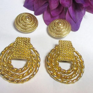 May include: A pair of gold-tone earrings with a circular design. The earrings feature a woven rope-like pattern and a square-shaped center piece.
