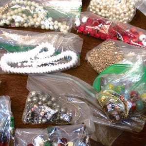 May include: Assortment of beads and jewelry components in clear plastic bags. Includes white, red, and iridescent beads, along with gold-toned metal embellishments. Ideal for crafting necklaces, bracelets, and other jewelry projects.
