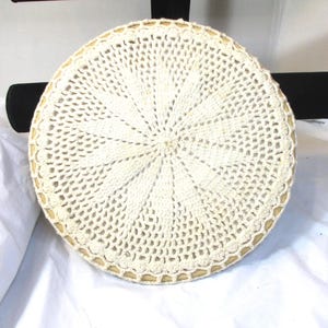 May include: Cream-colored, round crocheted doily with a detailed openwork pattern. The doily has a scalloped edge and a light tan border. The design radiates from the center, creating a starburst effect. This decorative item is suitable for home decor.