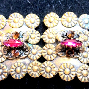 May include: Vintage gold-toned metal earrings with a floral design. Each earring features a large, faceted, pink gemstone and smaller brown gemstones. The earrings have a detailed, ornate design.