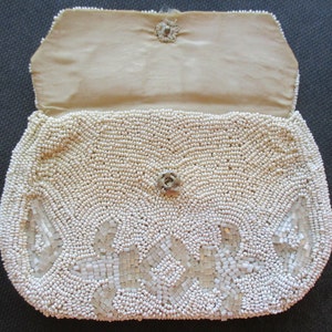 May include: A white beaded clutch bag with a floral design. The bag is open and the inside is lined with a cream-coloured fabric.