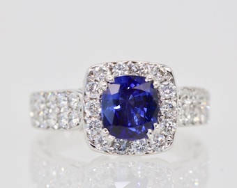 May include: A silver ring with a large, oval-shaped blue sapphire surrounded by a halo of smaller diamonds. The band of the ring is also set with diamonds.
