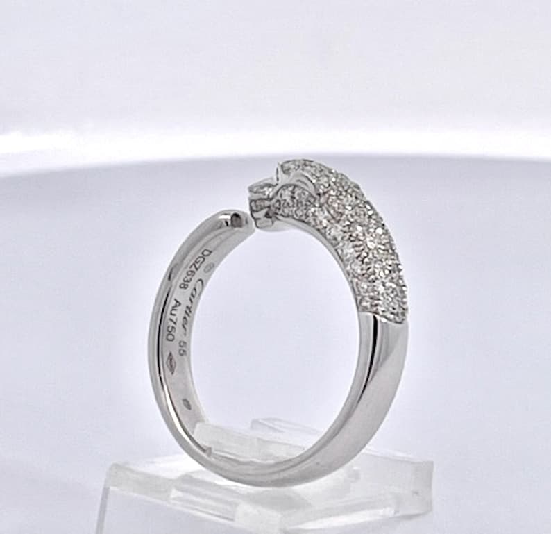 May include: A silver ring with a panther head design. The panther head is covered in small diamonds. The ring is engraved with the words 'Cartier' and '585 AU750'.