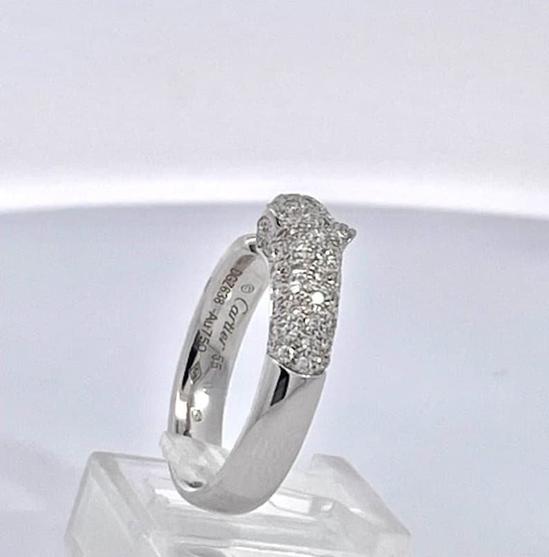 May include: A white gold ring with a pave diamond panther head design. The ring is engraved with 'Cartier 950 18K 002828'.