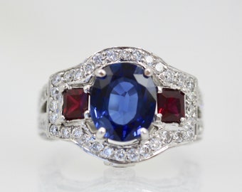 May include: A silver ring with a large blue sapphire surrounded by smaller diamonds. Two red rubies are set on either side of the sapphire.