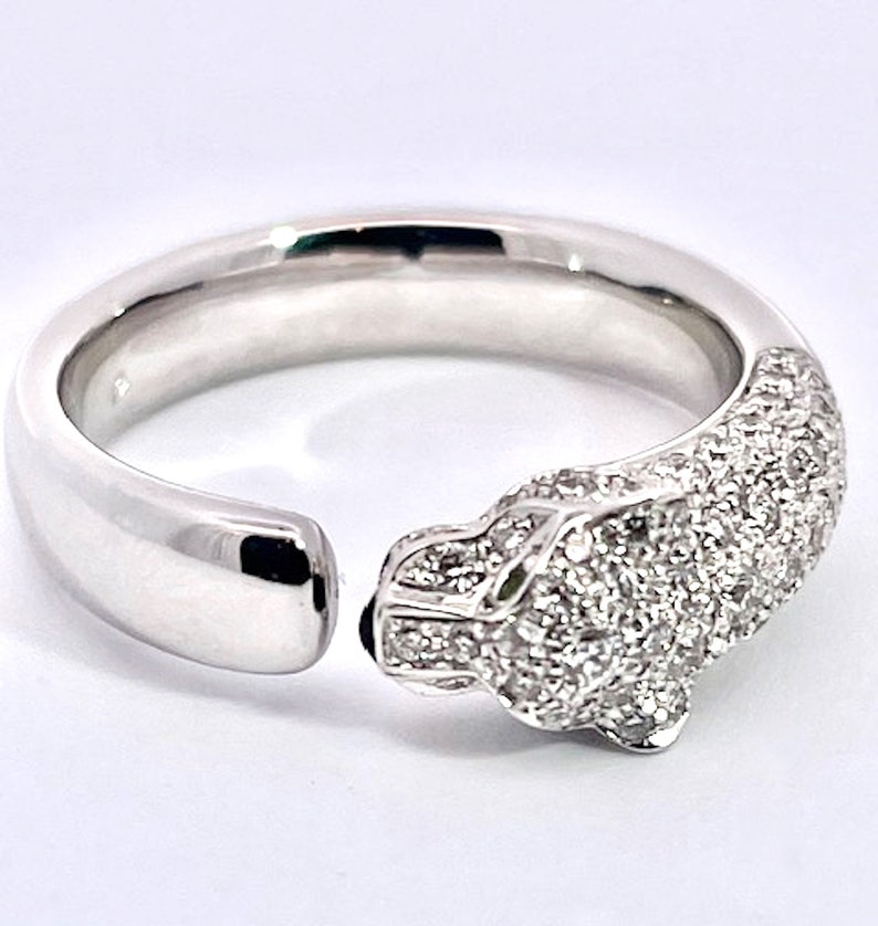 May include: A white gold ring with a diamond-encrusted panther head design. The ring is open on one side and the panther head is facing the right side of the image.