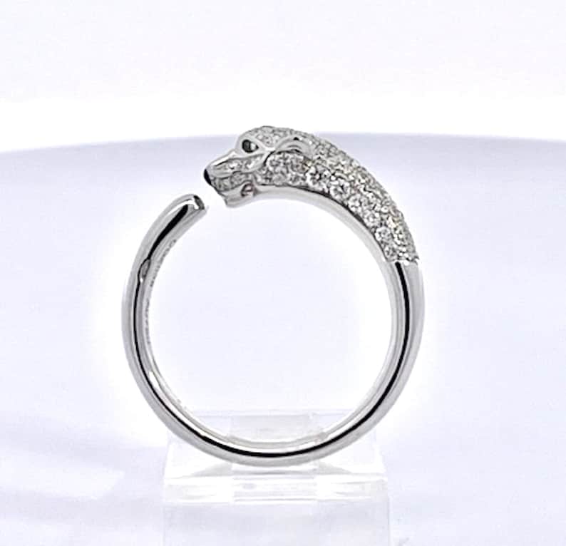 May include: A silver ring with a pave diamond panther head design. The panther's eyes are green gemstones.