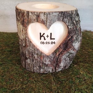 May include: A rustic wooden candle holder carved from a tree trunk. A heart is carved into the front, with the initials "K+L" and the date "08-21-24" inside. The candle holder is sitting on a bed of green moss.