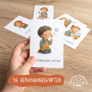 以下が含まれることがあります： 手は、シャボン玉を吹いている子供の水彩イラストが描かれたカードを持っています。他のカードには、さまざまな活動をしている子供たちが描かれています。「56 BERUHIGUNGSKARTEN」というテキストがオレンジ色のバナーに表示されています。