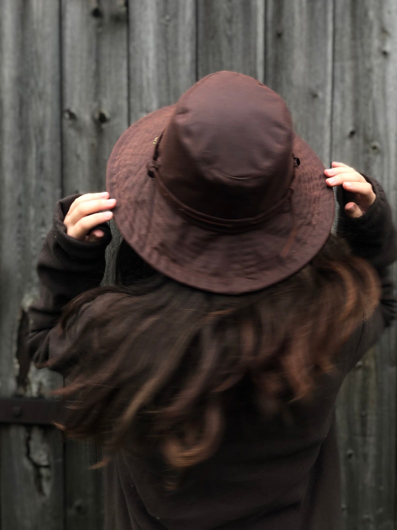 Puede incluir: Una persona con un sombrero marr&oacute;n de ala ancha y una chaqueta marr&oacute;n. El sombrero est&aacute; puesto bajo sobre la cabeza y el pelo es largo y oscuro.