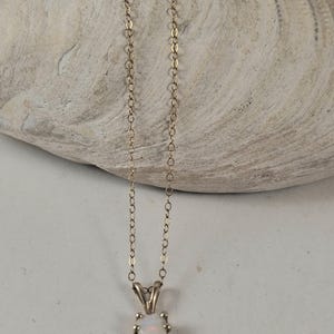 May include: A delicate gold chain necklace featuring a single pear-shaped opal pendant. The opal displays iridescent flashes of color and is secured in a simple metal setting. The thin, polished gold chain connects to the pendant at the top.