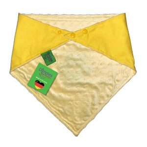 May include: A yellow baby bib with a soft, plush interior and a contrasting yellow exterior. The bib is secured with three yellow buttons and features a tag that reads "Dimples are happy" and "Made in Germany."