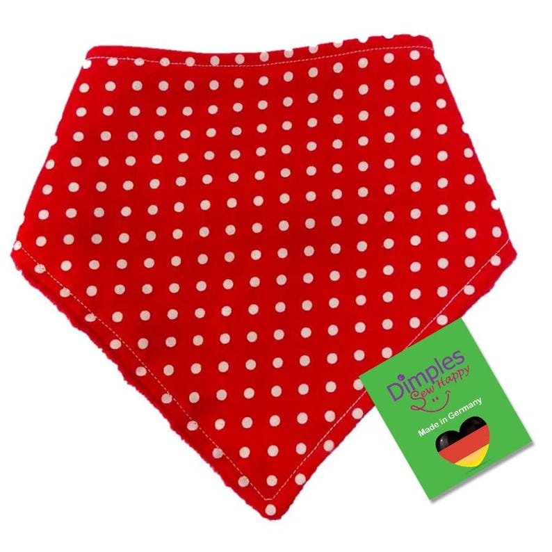 May include: A red bandana-style baby bib with white polka dots. The bib has a soft, fuzzy trim and a tag that reads "Dimples Sew Happy" and "Made in Germany."
