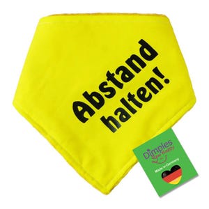 May include: A bright yellow bandana with the words "Abstand halten!" printed in bold black letters. A green tag with the text "Dimples Sew Happy" and a heart with the German flag is attached.