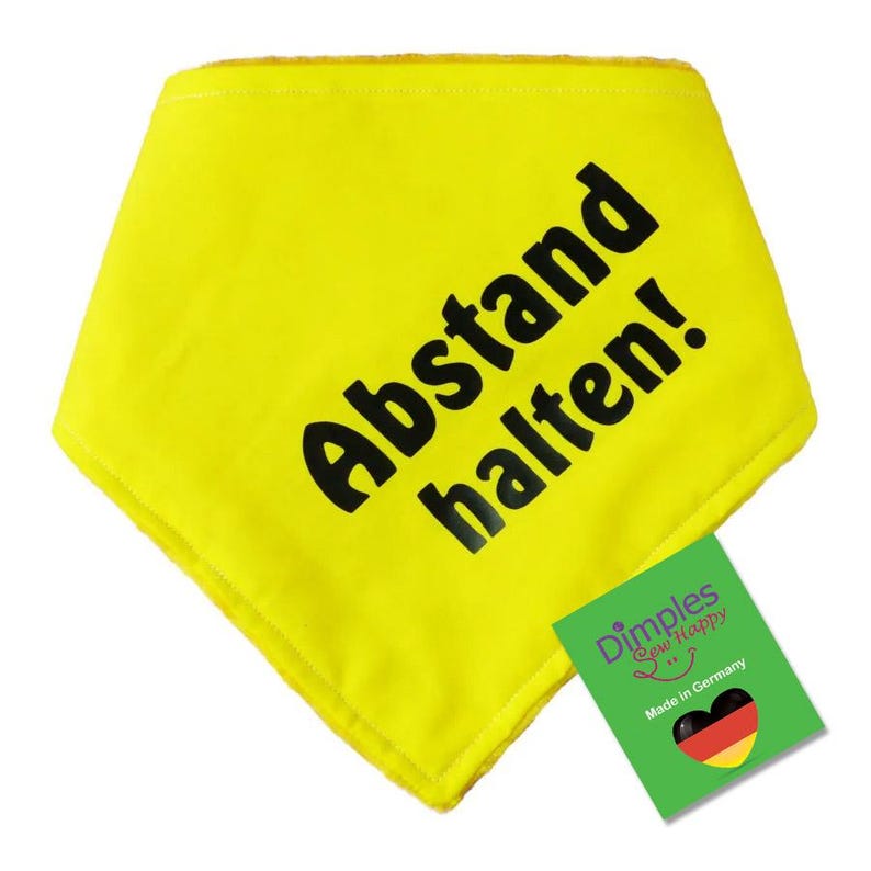 May include: A bright yellow bandana with the words "Abstand halten!" printed in bold black letters. A green tag with the text "Dimples Sew Happy" and a heart with the German flag is attached.