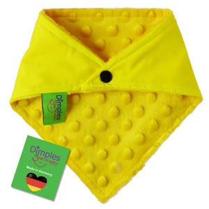 May include: Bright yellow baby bib with a textured, dotted pattern. The bib has a black button closure and a green tag that reads "Dimples Sew Happy" and "Made in Germany".