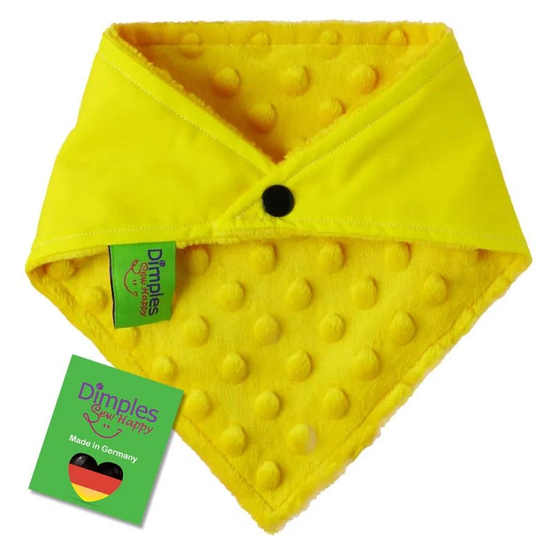 May include: Bright yellow baby bib with a textured, dotted pattern. The bib has a black button closure and a green tag that reads "Dimples Sew Happy" and "Made in Germany".