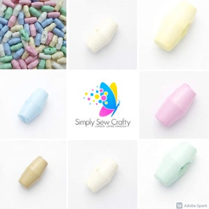 May include: Assortment of pastel coloured plastic toggle buttons. The buttons are in various shades of blue, green, pink, yellow, and white.  The buttons are shaped like a cylinder with a slight curve in the middle.  The buttons are approximately 2.5 cm long.