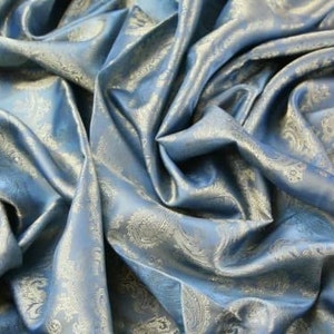 Op de afbeelding: Een blauwe stof met een wit paisley-patroon. De stof is zacht en zijdeachtig en heeft een subtiele glans.