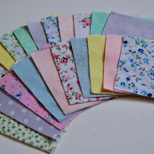 Può includere: Una collezione di 16 quadrati di tessuto in vari colori pastello e motivi floreali. I quadrati sono disposti a ventaglio, con i colori più chiari in alto e i colori più scuri in basso.