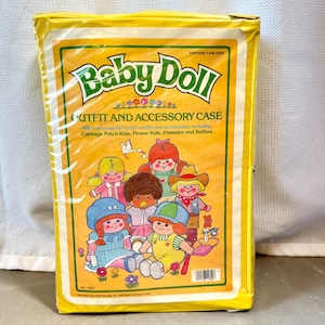 May include: A yellow rectangular Baby Doll Outfit and Accessory Case in plastic packaging. The front features illustrations of five dolls and text stating it holds 16 to 18 inch outfits for Cabbage Patch Kids, Flower Kids, Preemies, and Softina.