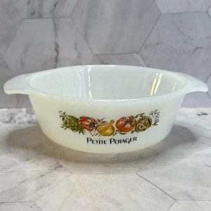 May include: A white milk glass bowl with two side handles, featuring a colorful vegetable illustration of an artichoke, pepper, onion, and tomato, with the black text PETITE POTAGER printed centered below the vegetable graphic design.