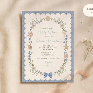 May include: A rectangular baby shower invitation card with a scalloped blue border. The centre features a floral and seashell wreath surrounding text that reads Join us for a Baby Shower in honour of Olivia Alexander, Saturday December 5, 2026.
