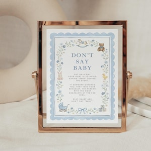 May include: A gold-toned metal frame holding a sign with a light blue scalloped border. The sign features illustrations of a rocking horse, teddy bear, rabbit, duck, stroller, and blocks, with the text DON'T SAY BABY and game instructions.