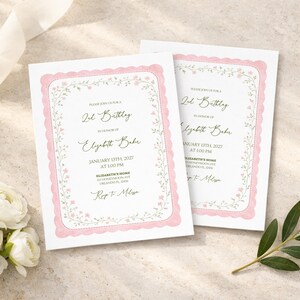 May include: Two birthday invitations with a pink scalloped border and floral accents. The text reads "2nd Birthday" and includes the name "Elizabeth Baker" and event details. White flowers and a ribbon are in the background.