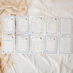 May include: A set of nine rectangular baby shower game cards with light blue scalloped borders, featuring illustrations of teddy bears, rocking horses, and floral motifs. The cards include titles like Predictions for Baby Boy, Who Knows Mommy Best, and Baby Gift Bingo.