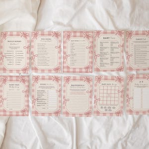 Op de afbeelding: Een verzameling babyshower-spelkaarten met een roze ruitpatroon en roze strikaccenten. De kaarten bevatten verschillende speltitels zoals "Would Mommy Rather?" en "Baby Trivia". De kaarten zijn gerangschikt op een witte ondergrond.