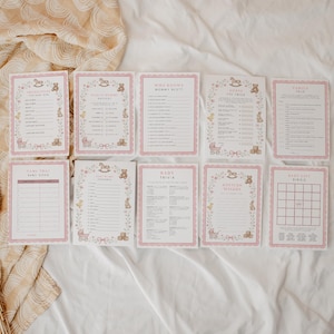 May include: A set of ten rectangular baby shower game cards with pink scalloped borders, featuring illustrations of teddy bears, rocking horses, and baby carriages. The cards include titles like Baby Song, Baby Trivia, and Baby Gift Bingo in black text.