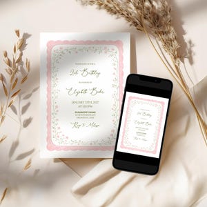 May include: A printed invitation with a pink scalloped border and floral accents, displayed next to a smartphone showing the same design. The invitation text reads "2nd Birthday" and includes event details. Dried plants are in the background.