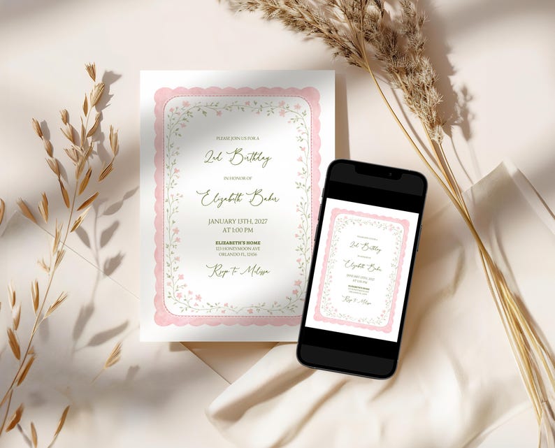 May include: A printed invitation with a pink scalloped border and floral accents, displayed next to a smartphone showing the same design. The invitation text reads "2nd Birthday" and includes event details. Dried plants are in the background.