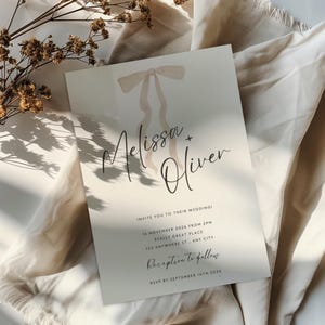 Puede incluir: Una invitación de boda con una ilustración de acuarela de un lazo. La invitación es para la boda de Melissa y Oliver el 16 de noviembre de 2024 a las 2 PM. La recepción seguirá en 123 Anywhere St., Any City. RSVP antes del 16 de septiembre de 2026.