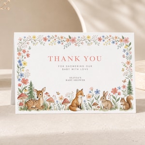 Peut inclure: Une carte de remerciement blanche avec une bordure florale et des animaux des bois, dont un cerf, un renard, un lapin et un écureuil avec des champignons. Le texte indique : THANK YOU FOR SHOWERING OUR BABY WITH LOVE OLIVIA'S BABY SHOWER.