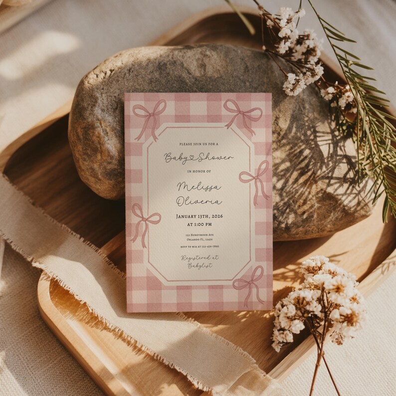 May include: A baby shower invitation with a pink gingham pattern and bow accents. The invitation includes the text "Please join us for a Baby Shower in honor of Melissa Oliveria, January 13th, 2026 at 1:00 PM."