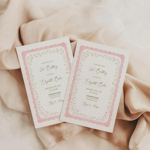 May include: Two pink and white birthday invitations with floral borders. The invitations include the text "2nd Birthday" and event details. The cards are displayed on a soft, peach-colored fabric.