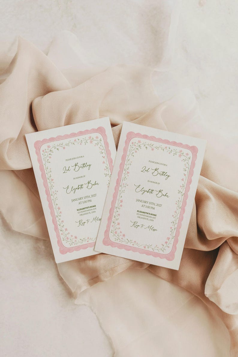 May include: Two pink and white birthday invitations with floral borders. The invitations include the text "2nd Birthday" and event details. The cards are displayed on a soft, peach-colored fabric.