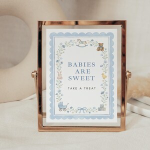 May include: A rectangular rose gold metal frame holding a white sign with a scalloped light blue border. The sign features blue text reading BABIES ARE SWEET TAKE A TREAT, surrounded by illustrations of a rocking horse, teddy bear, rabbit, duck, and carriage.