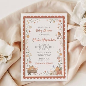 May include: A rectangular baby shower invitation card with a scalloped terracotta border. The design features illustrations of pumpkins, flowers, and a bird. Text includes: Join us for a Baby Shower in honor of Olivia Alexander, Saturday October 24, 2026.
